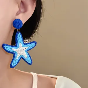 Close-up detail of blue and white woven star-shaped drop earrings on model
