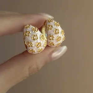 Close-up of retro C-shaped earrings with pink enamel and gold floral diamond studs.
