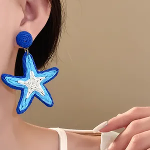 Woven blue and white starfish earrings worn by a model for a beachy summer look.