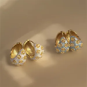 Detailed view of vintage gold hoop earrings with white and blue enamel flower inlay