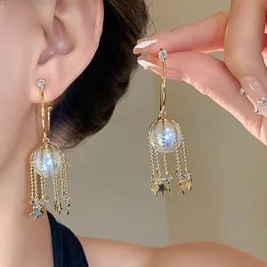 Vue détaillée de boucles d'oreilles créoles C dorées avec perles et pampilles étoiles.