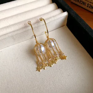Gros plan détaillé de boucles d'oreilles en C dorées avec perles et glands d'étoiles.
