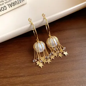 Gros plan de boucles d'oreilles créoles dorées en C avec perles et glands d'étoiles
