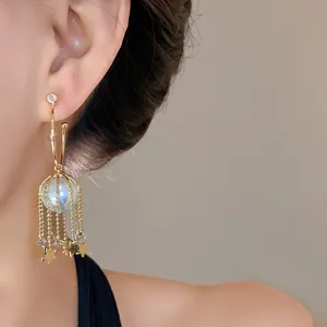 Gros plan de boucles d'oreilles créoles en C avec perle et glands étoiles dorées pendants.