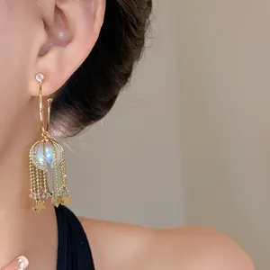 Détail de boucles d'oreilles dorées en C avec perles et glands d'étoiles sur l'oreille du mannequin