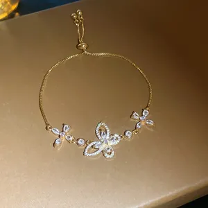Close-up of a gold-plated bracelet with a sparkling zircon butterfly and flower charms.