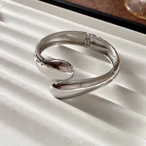 Vista detallada de un brazalete de metal plateado con un elegante diseño de gota de agua
