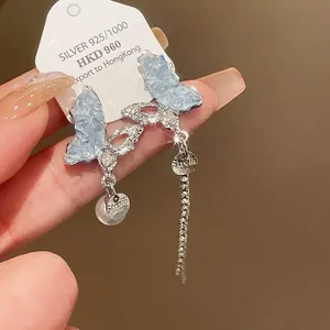 Detailed macro shot of blue crystal butterfly earrings with dangling pearl and silver tassel