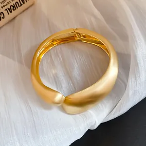 Primer plano de un brazalete escultural ancho en oro mate con textura de metal cepillado.