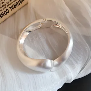 Vista detallada de un brazalete de metal plateado mate minimalista con un cierre de bisagra