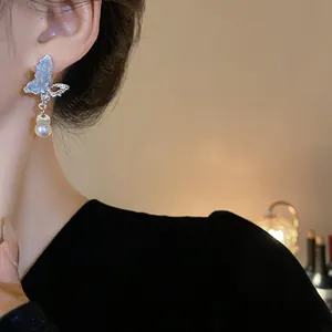 Close-up of butterfly drop earrings with shimmering crystals and a white pearl.