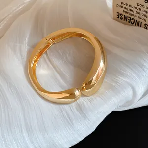 Primer plano de un brazalete metálico irregular dorado sobre tela blanca texturizada
