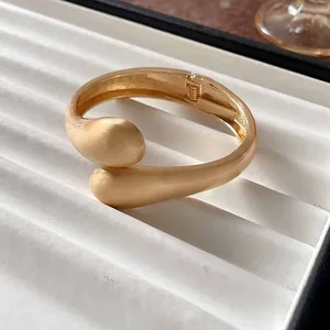 Detalle macro de brazalete de gota en oro mate sobre bandeja de joyas