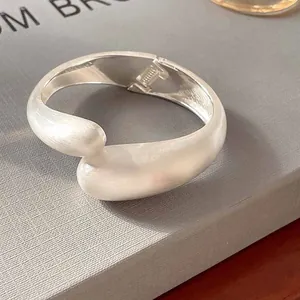 Primer plano de un brazalete escultórico de metal plateado con acabado cepillado.