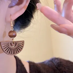 Detailed close-up of a bohemian hollow fan wood pendant earring on a model's ear