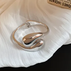 Detalle de un brazalete metálico plateado con un diseño de lágrima vanguardista único.