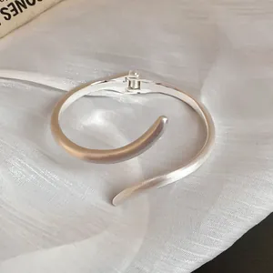 Detalle macro de un brazalete de bisagra curvo plateado sobre tela blanca suave
