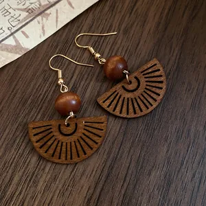 Close-up of Bohemian fan-shaped hollow wood earrings with brown beads on dark wood.