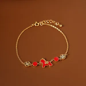 Detailed macro view of a gold-plated bracelet with red enamel horse charm and clear stones