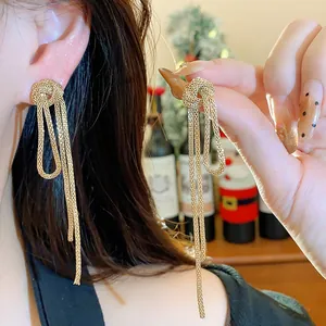 Detailed view of elegant gold chain knot tassel earrings being worn and held by a model.
