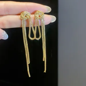 Close-up detail of elegant gold-toned knot earrings featuring long mesh chain tassels