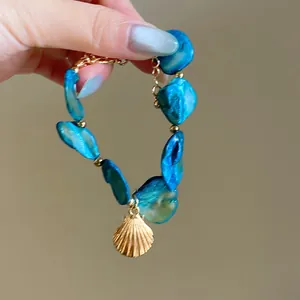 Macro detail view of a blue irregular pearl bracelet featuring a gold shell pendant