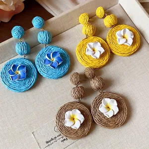 Handmade raffia woven flower earrings with polymer clay frangipani in blue and yellow.