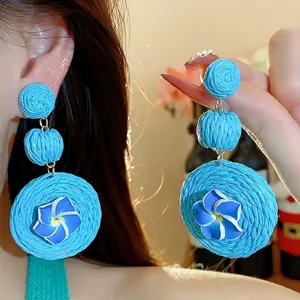 Handmade blue raffia woven drop earrings featuring polymer clay plumeria flowers on an Asian model