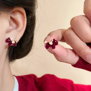 Primer plano de pendientes de caballo flocado burdeos con detalles dorados y aguja plata.