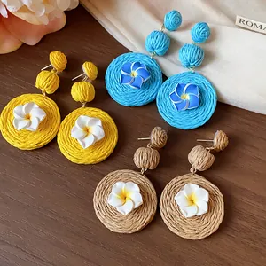 Close-up detail of bohemian raffia tiered earrings featuring delicate white clay flowers