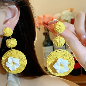 Close-up of handmade yellow raffia earrings with white clay flowers and silver pins.