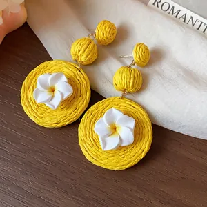 Close-up of yellow woven raffia earrings with white flower detail in vacation style.