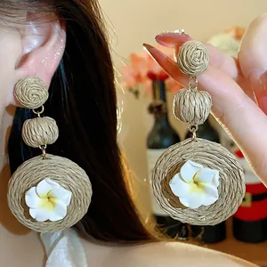 Close-up of bohemian raffia earrings featuring delicate white polymer clay flowers.