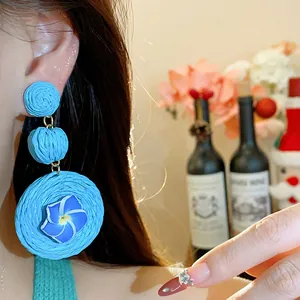 Detail view of blue raffia drop earrings with polymer clay flower on a model's ear