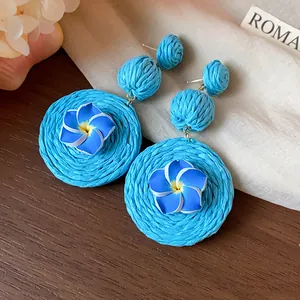 Close-up detail of blue raffia woven earrings with delicate polymer clay flowers.
