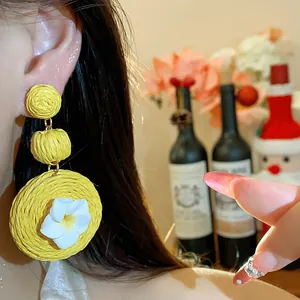 Detail close-up of yellow raffia earrings with a white clay flower on an Asian model.
