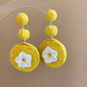 Detail shot of yellow raffia woven earrings featuring delicate white clay flowers