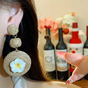 Macro detail of raffia woven drop earring with a delicate white polymer clay flower.