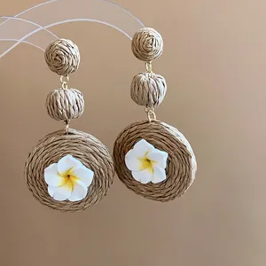 Detailed close-up of woven raffia drop earrings with white frangipani flowers.