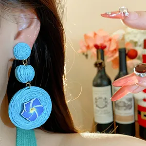 Detail shot of blue raffia woven earrings with a delicate blue flower on model's ear