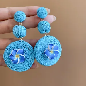 Detailed view of handmade blue raffia woven earrings with polymer clay flower accents