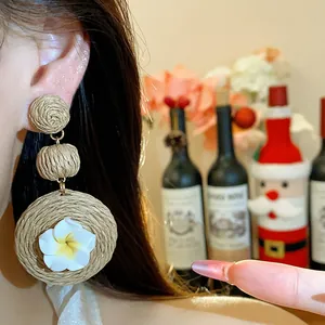 Close-up view of bohemian raffia woven earrings with white polymer clay flower detail on model