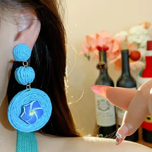 Close-up of light blue woven raffia earrings with a delicate clay flower center.
