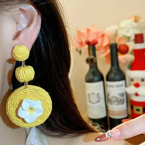 Detail of yellow raffia earrings with white flower and silver needle design.