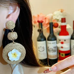 Close-up of handmade raffia earrings with plumeria flower detail worn by model