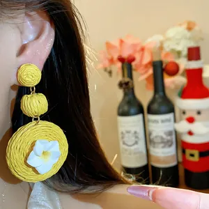 Detailed view of yellow raffia woven earrings with a delicate white clay flower worn on the ear.