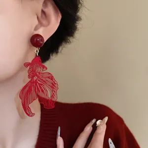 Detailed close-up of a red hollow goldfish earring worn by a model in Chinese style.