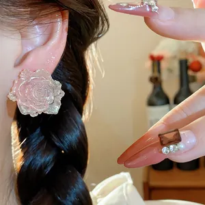 Close-up detail view of pink resin rose flower stud earring with silver needle on model ear