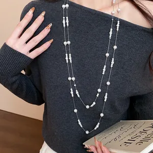Dettaglio di un'elegante collana di perle a doppio strato su maglia grigia a coste