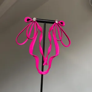 Hot pink ribbon bow earrings with rhinestone studs on a minimalist display stand